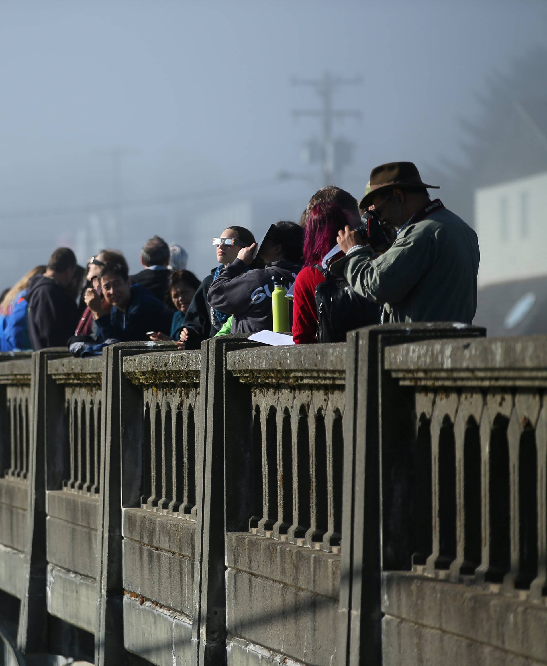 People line up on a bridge as the sun emerges through fog cover before the solar eclipse in Depoe Bay