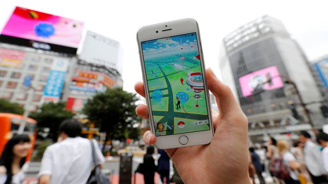 A man poses with his mobile phone displaying the augmented reality mobile game "Pokemon Go" by Nintendo in front of a busy crossing in Shibuya district in Tokyo