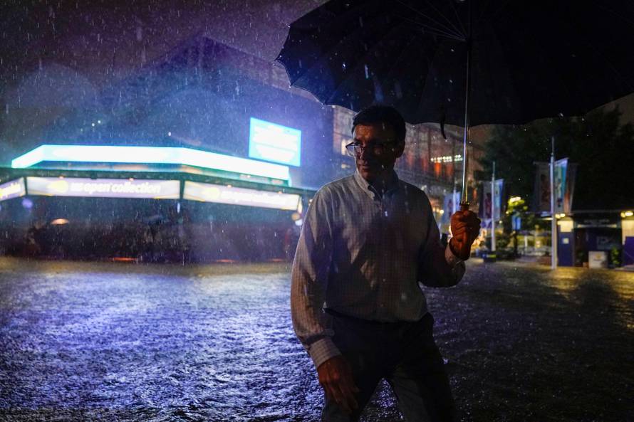 A spectator walks through the flooded pavilion in front of Louis Armstrong Stadium