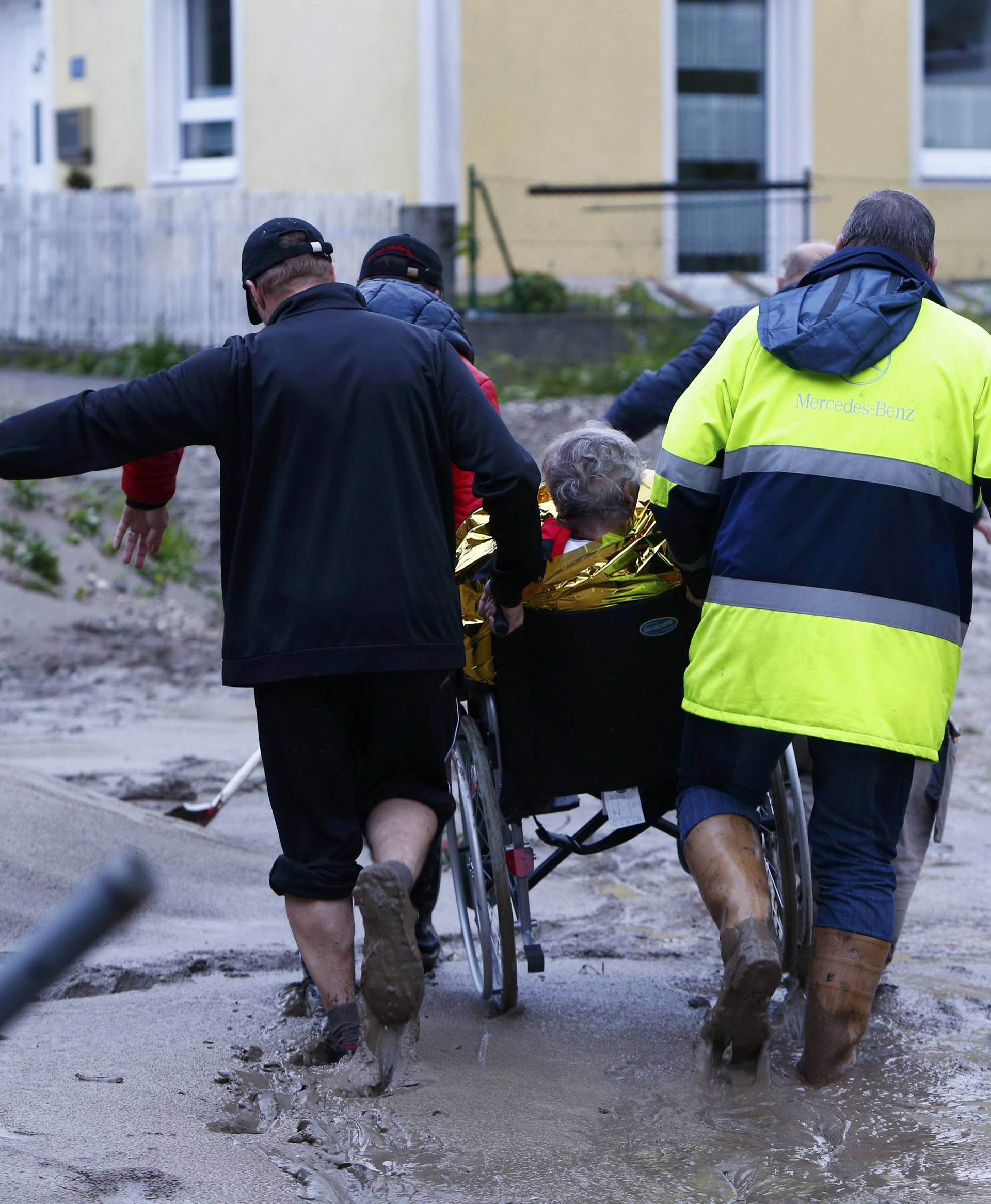 People carry an elderly woman on a wheelchair over mud covered street after floods in the Bavarian village of Simbach am Inn