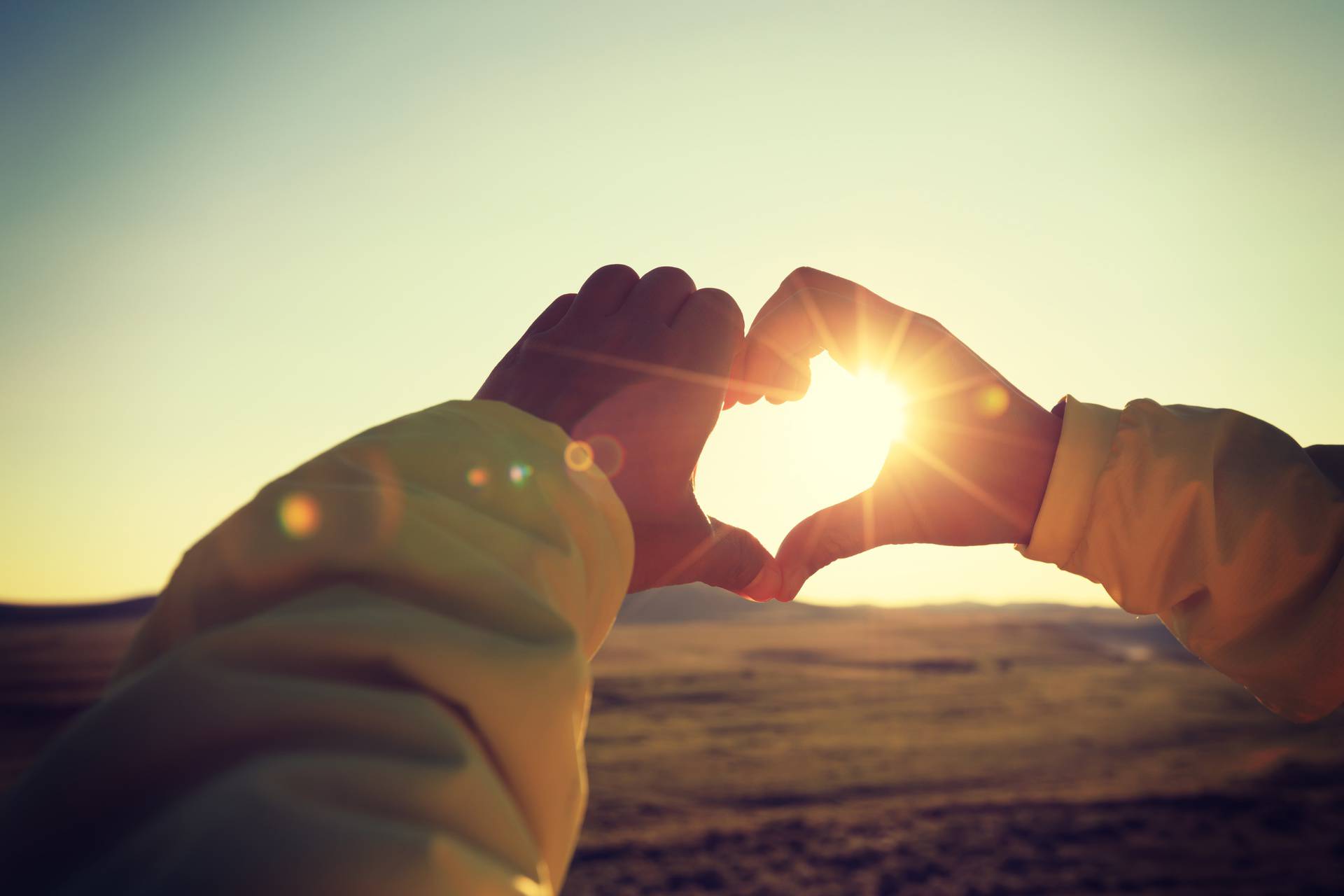 Human hands making Heart shaped sign over sunset sky