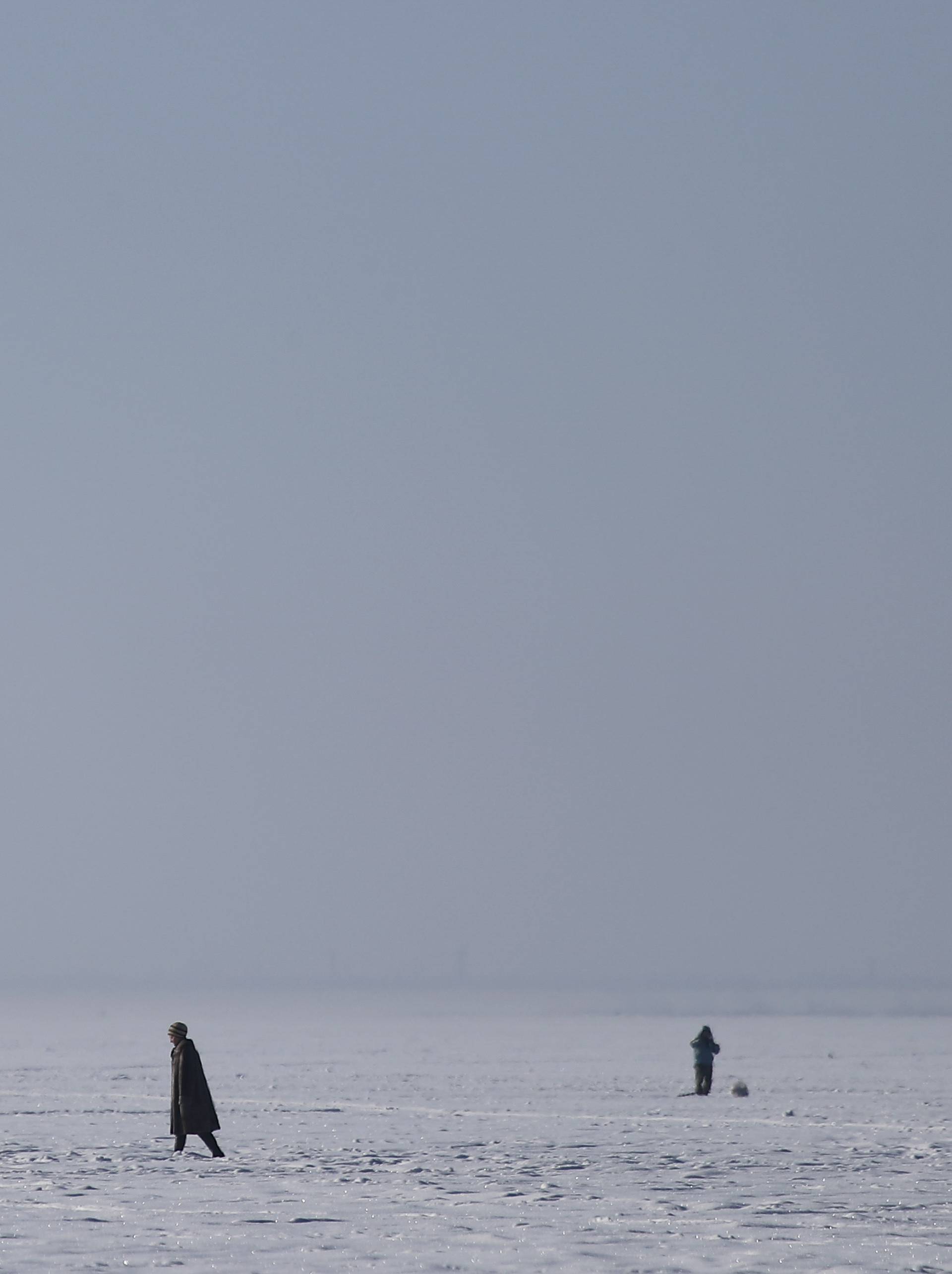 A woman passes a fisherman on the ice-covered Gulf of Finland on the outskirts of St. Petersburg