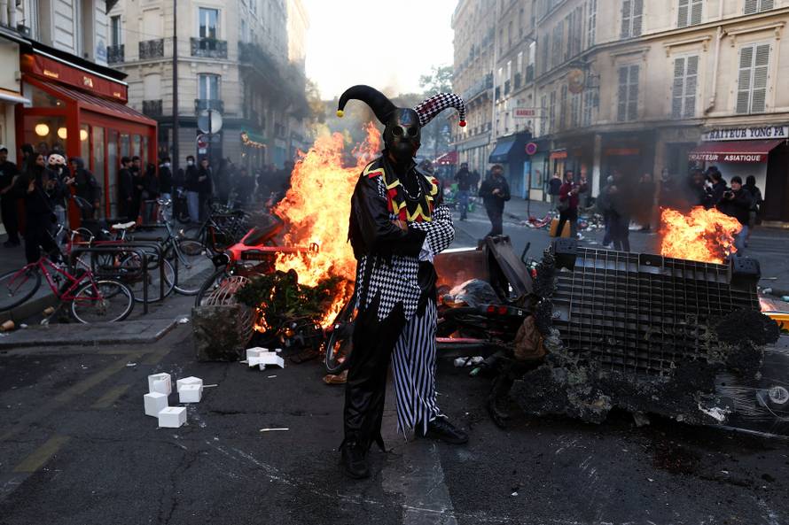 A demonstrator wearing a costume stands in front of burning flames, in Paris