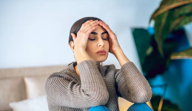 Dark-haired woman sitting on bed and looking frustrated