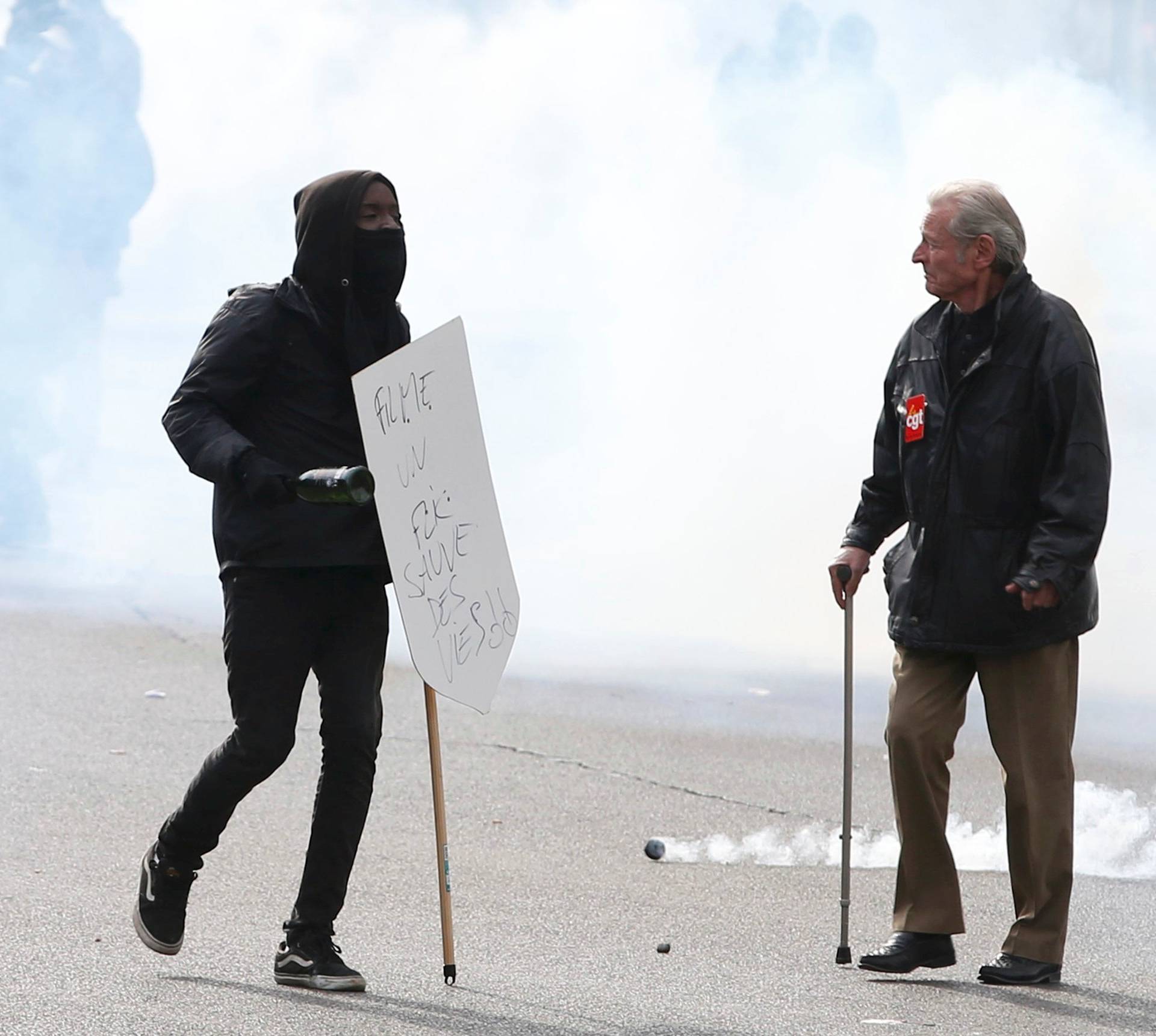 A masked youth and a demonstrator walk through a cloud of tear gas during a demonstration against the French labour law proposal in Paris