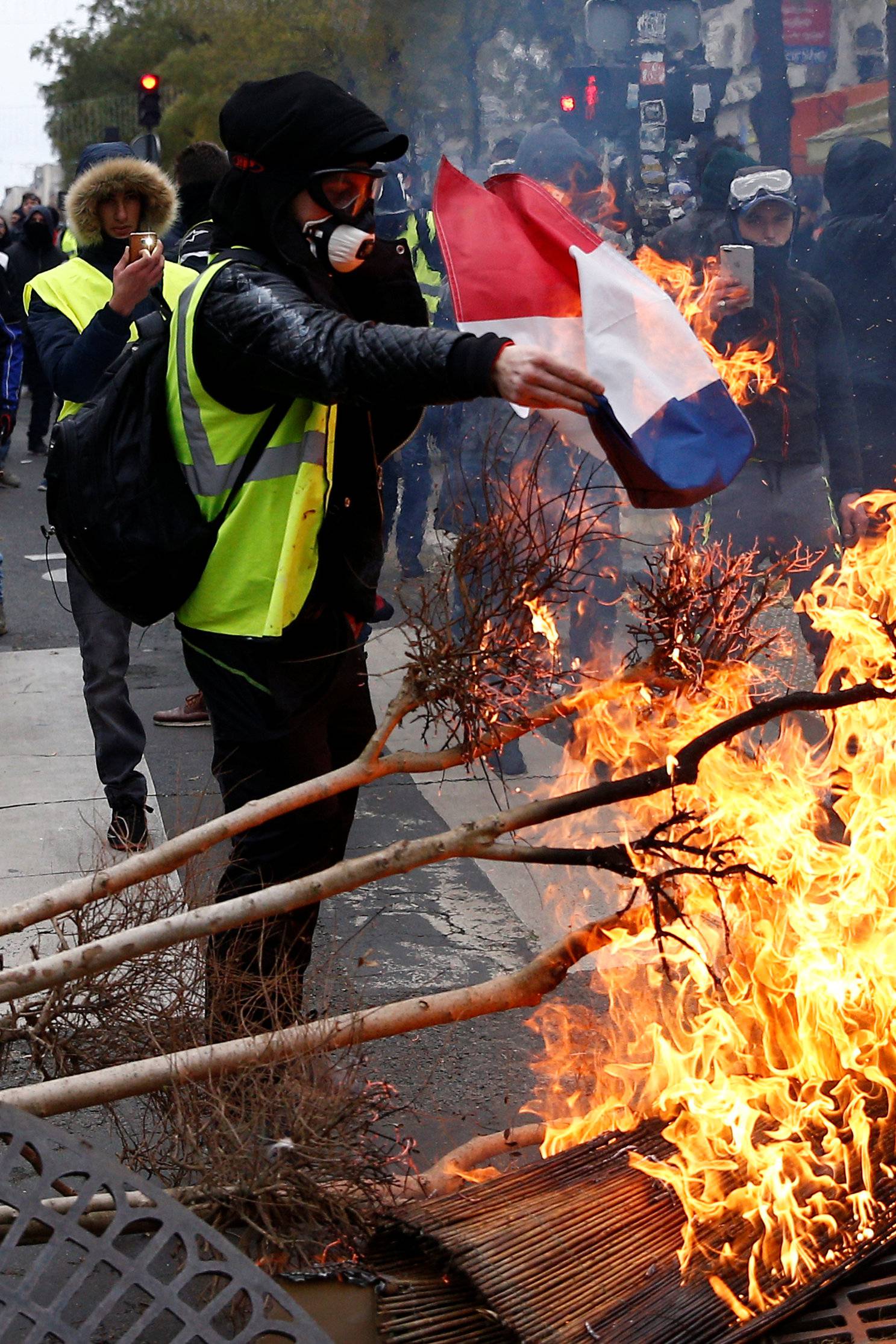 A protester wearing a yellow vest burns a French flag at a barricade during clashes with police as part of a national day of protest by the "yellow vests" movement in Paris