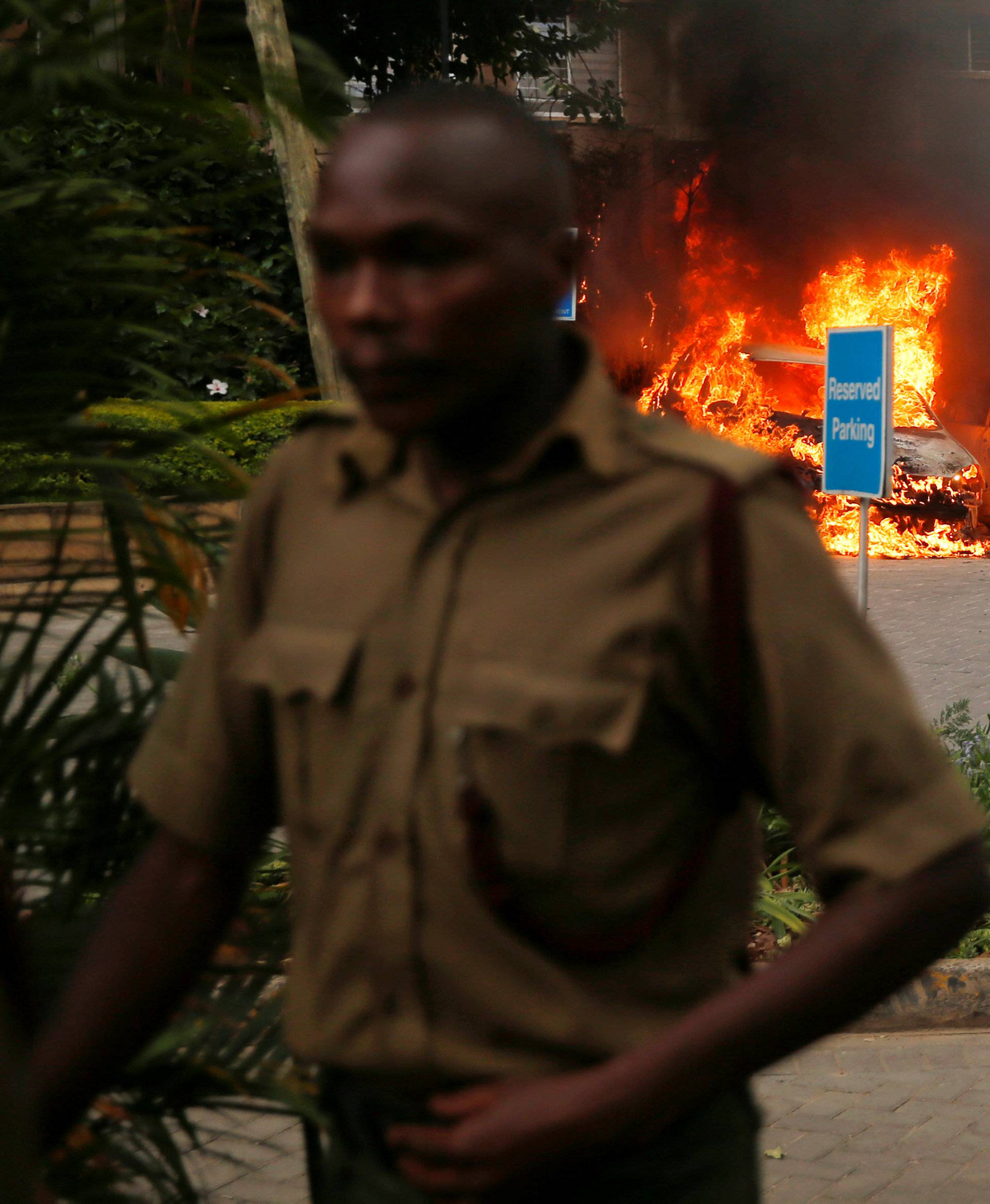 A policeman runs past burning cars at the scene where explosions and gunshots were heard at the Dusit hotel compound, in Nairobi