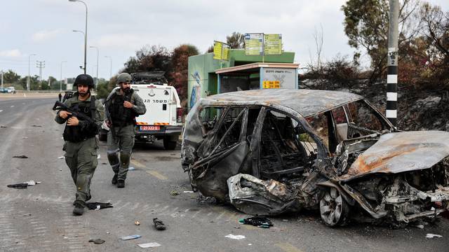 Israeli border police walk past a burnt out car as rockets are launched from the Gaza Strip towards Israel, in Ashkelon, southern Israel