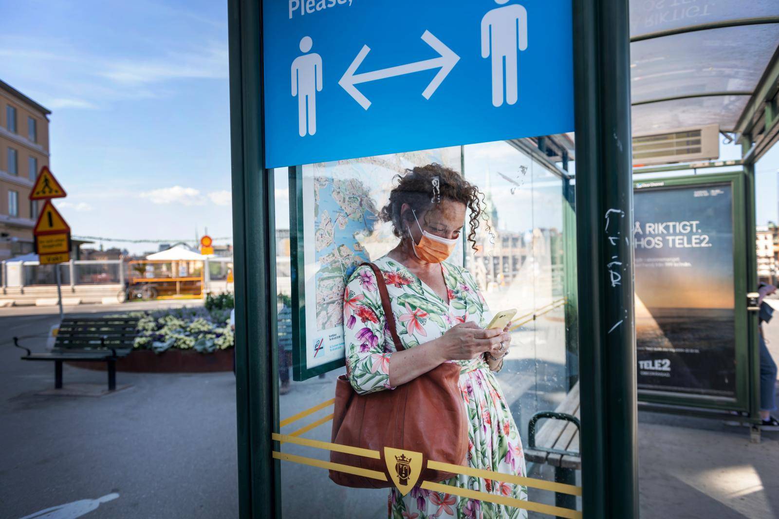 A woman wearing a face mask is seen in a bus stop next to an information sign asking people to keep social distance due to the outbreak of coronavirus disease (COVID-19), in Stockholm