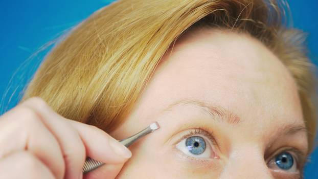 Extreme close-up. plucking eyebrows tweezers, a blonde girl with blue eyes pulls out unnecessary hairs from her eyebrow
