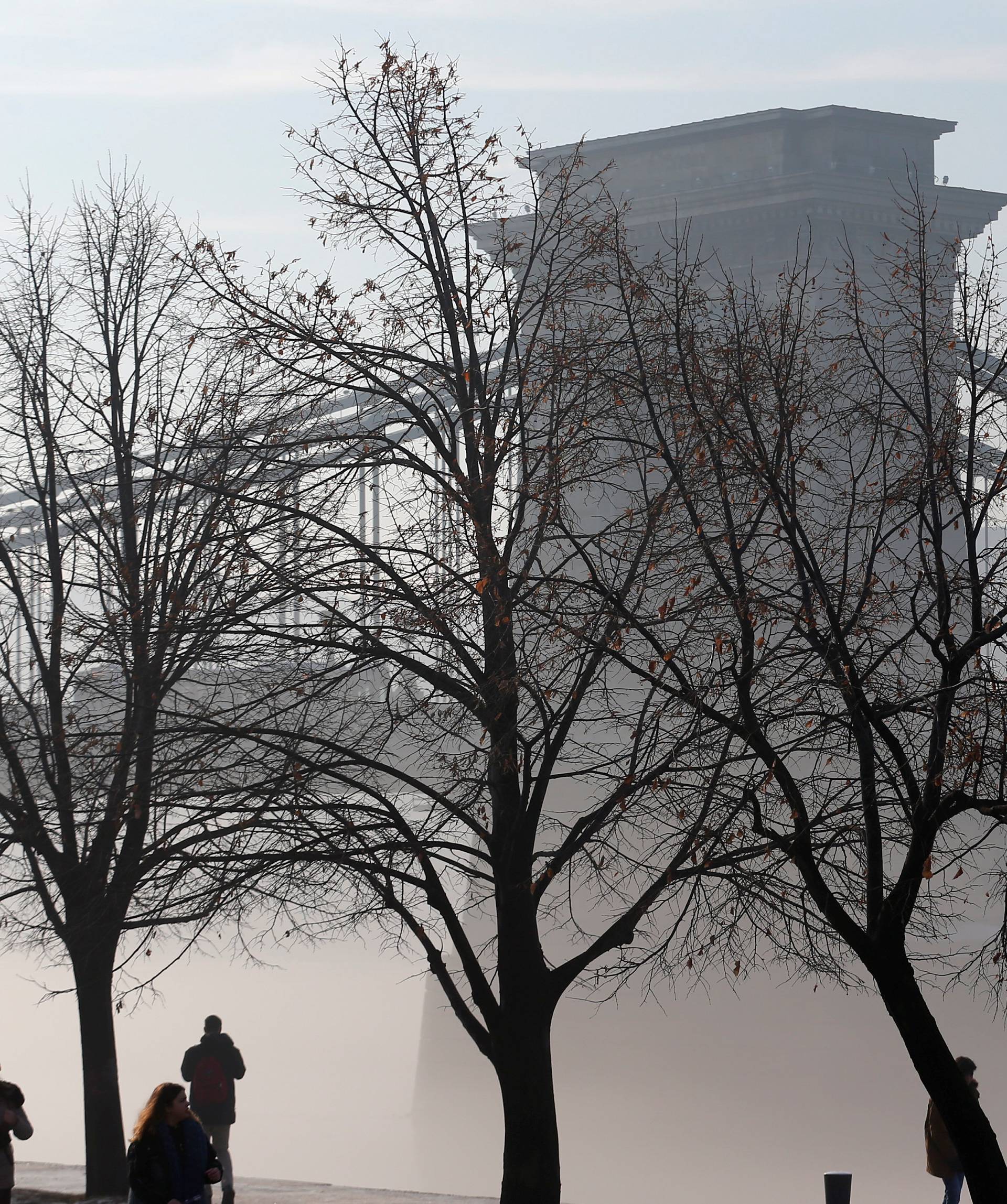 People walk front of the Chain Bridge which is wrapped in a veil of fog as the sun rises above the Danube river in Budapest