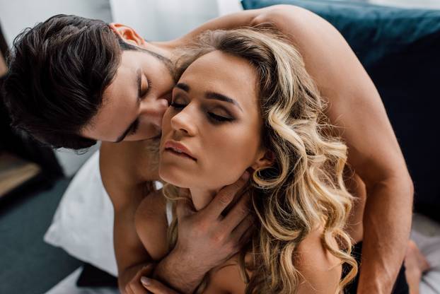 Handsome man kissing and touching neck of sexy girlfriend on bed