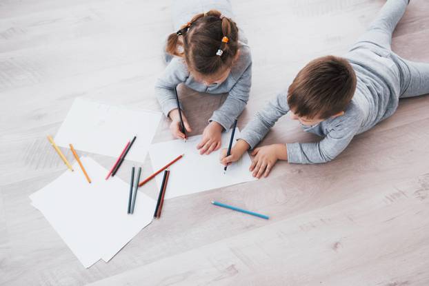 Children lie on the floor in pajamas and draw with pencils. Cute child painting by pencils