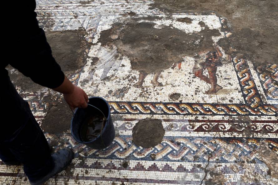 An Israel Antiquities Authority worker holds a bucket while cleaning a mosaic floor decorated with figures, which archaeologists say is 1,800 years old and was unearthed during an excavation in Caesarea
