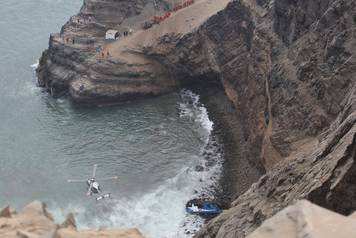 A helicopter helps rescue workers at the scene after a bus crashed with a truck and careened off a cliff along a sharply curving highway north of Lima