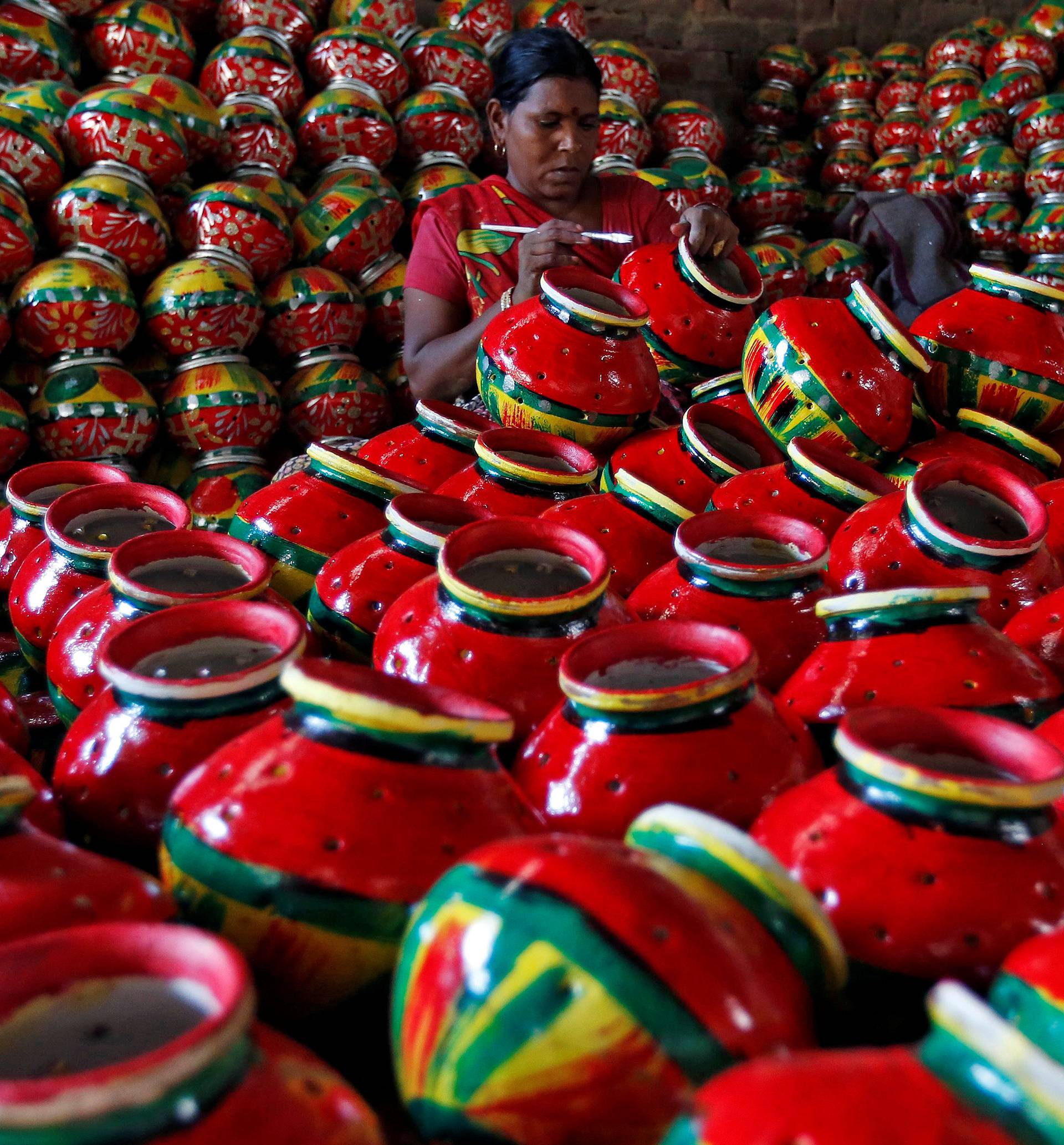Woman decorates an earthen pitcher typically used during Garba, a folk dance, inside a workshop ahead of Navratri in Ahmedabad