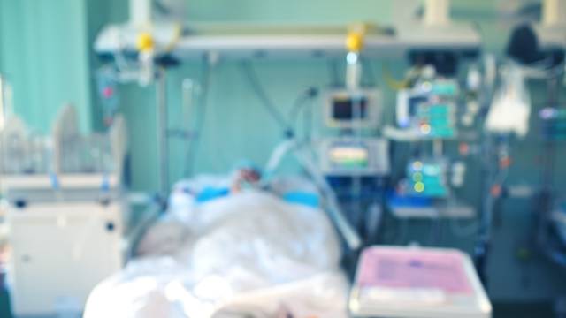 Defocused hospital background with patient connected to the advanced life support equipment in the intensive care unit.