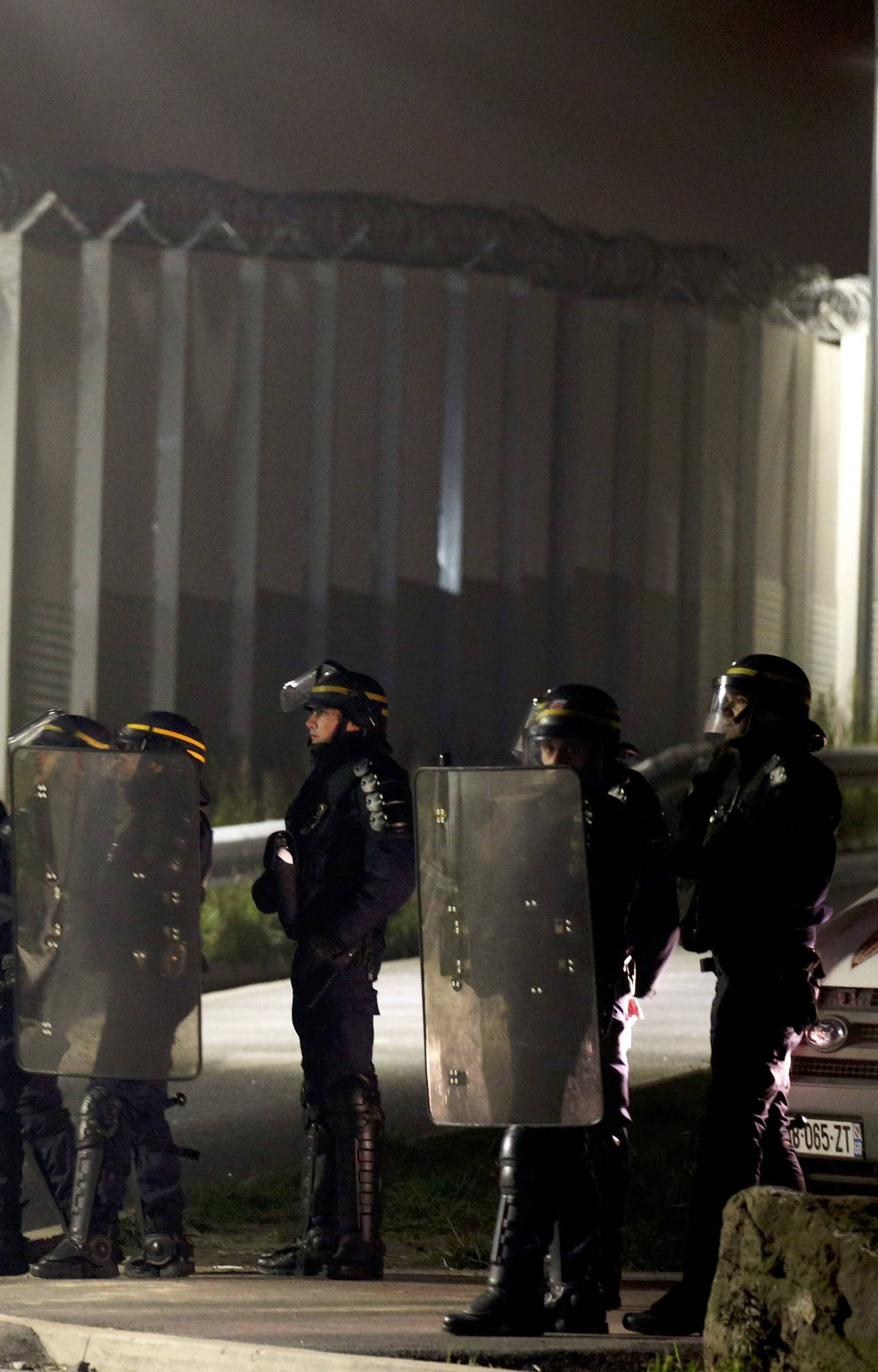 French CRS riot police stand by the razor-wire topped fence which secures the road approach to the city and dissuades migrants from trying to reach Britain on lorries on the eve of the evacuation and dismantlement of the camp called the "Jungle" in Calais