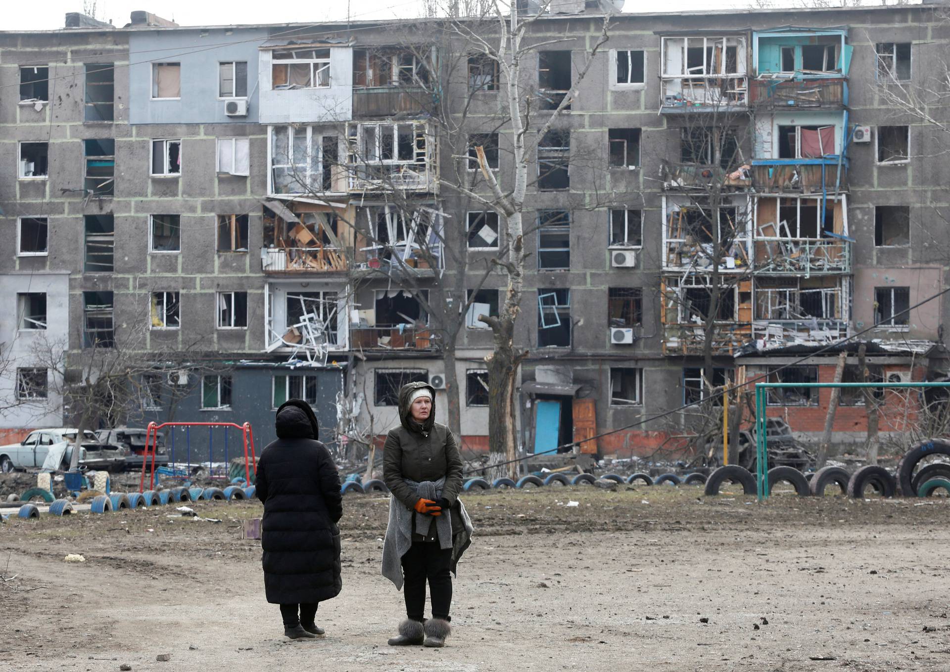 Local residents stand in front of a damaged residential building in the besieged city of Mariupol