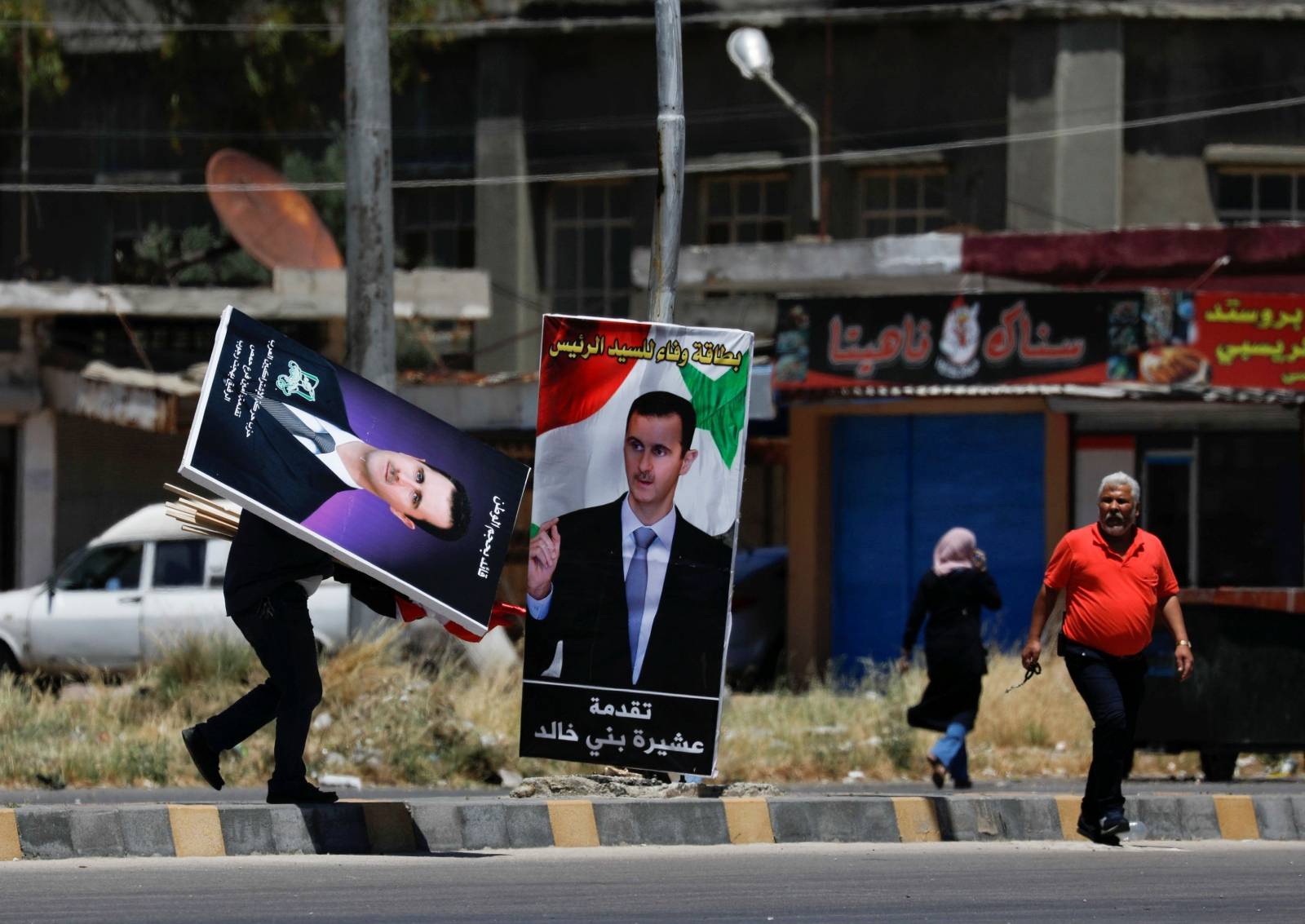 A man walks as he carries posters depciting Syria's President Bashar al-Assad, in the district of al-Waer