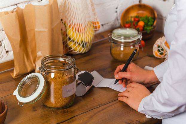 woman hand is writing name of product to stick on glass jar conscious shopping no plastic