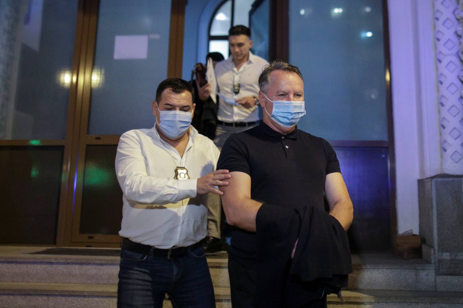 Police officers, wearing masks against the new coronavirus disease (COVID-19), escort Laurentiu Baranga, former chief of Romania's agency for the prevention and control of money laundering, to a police car