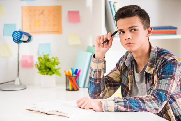 Male,Teenager,Sitting,At,The,Table,And,Holding,A,Pen