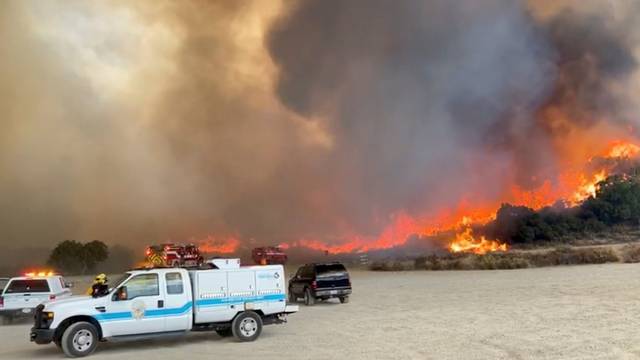 Vehicles of San Diego Humane Society's Emergency Response Team and fire engines of San Diego County Fire are seen as the Valley Fire rages in the background in San Diego, California
