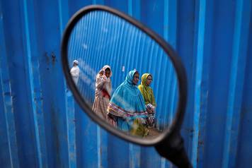 Dawoodi Bohra Muslims are reflected in the rear mirror of a parked scooter as they walk past the site of an under construction mosque in Mumbai