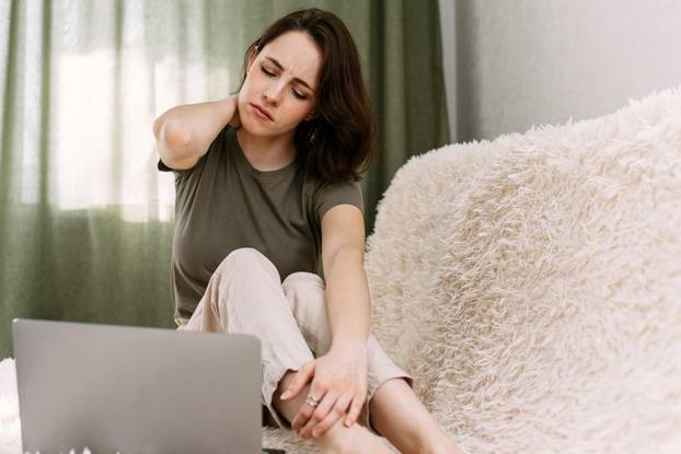 A business woman suffering from pain in neck, stretching up. Tired woman massaging rubbing stiff sore neck tensed muscles fatigue from computer work. Freelancer tired of working at home on the couch