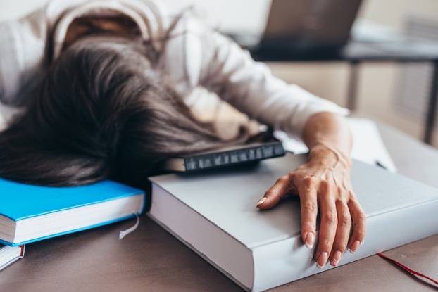 Tired woman sleeping on table face and hands on books