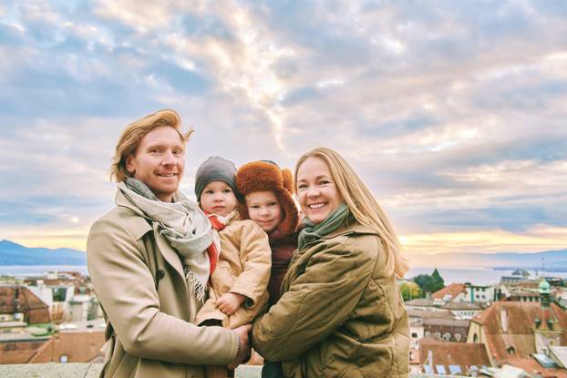   Outdoor portrait of happy family of four, young couple with two little children, cold weather, old european city on background