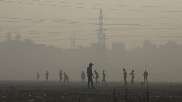 People play cricket on the floodplains of the Yamuna river on a smoggy morning in New Delhi
