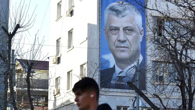 Man walks near a banner displaying former Kosovo President Hashim Thaci, in Pristina