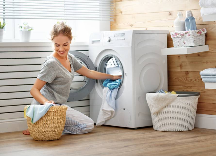 Happy housewife woman in laundry room with washing machine  