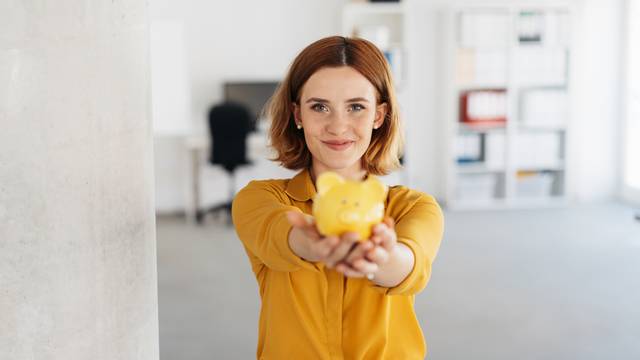 Smiling,Successful,Young,Woman,Holding,A,Piggy,Bank,Extended,To