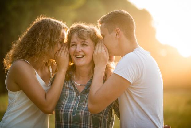 Daughter and son whispering secret into mother's ear