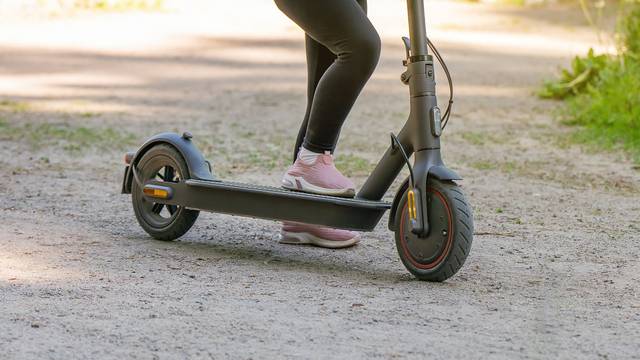 Little girl rides an electric scooter on a dirt road in the park.