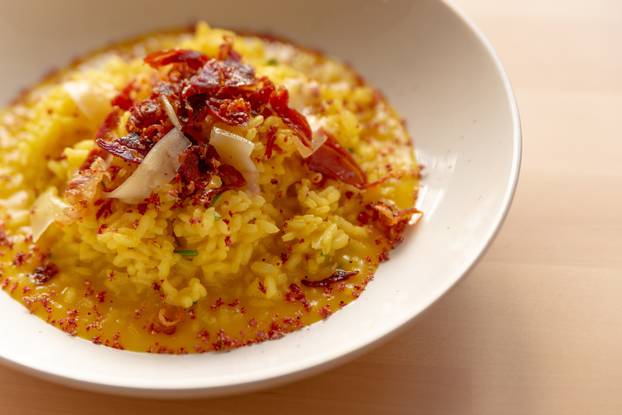 saffron risotto close up, classic yellow colorful italian food staple dish on white plate on wooden table with speck, a gourmet sophisticated presentation