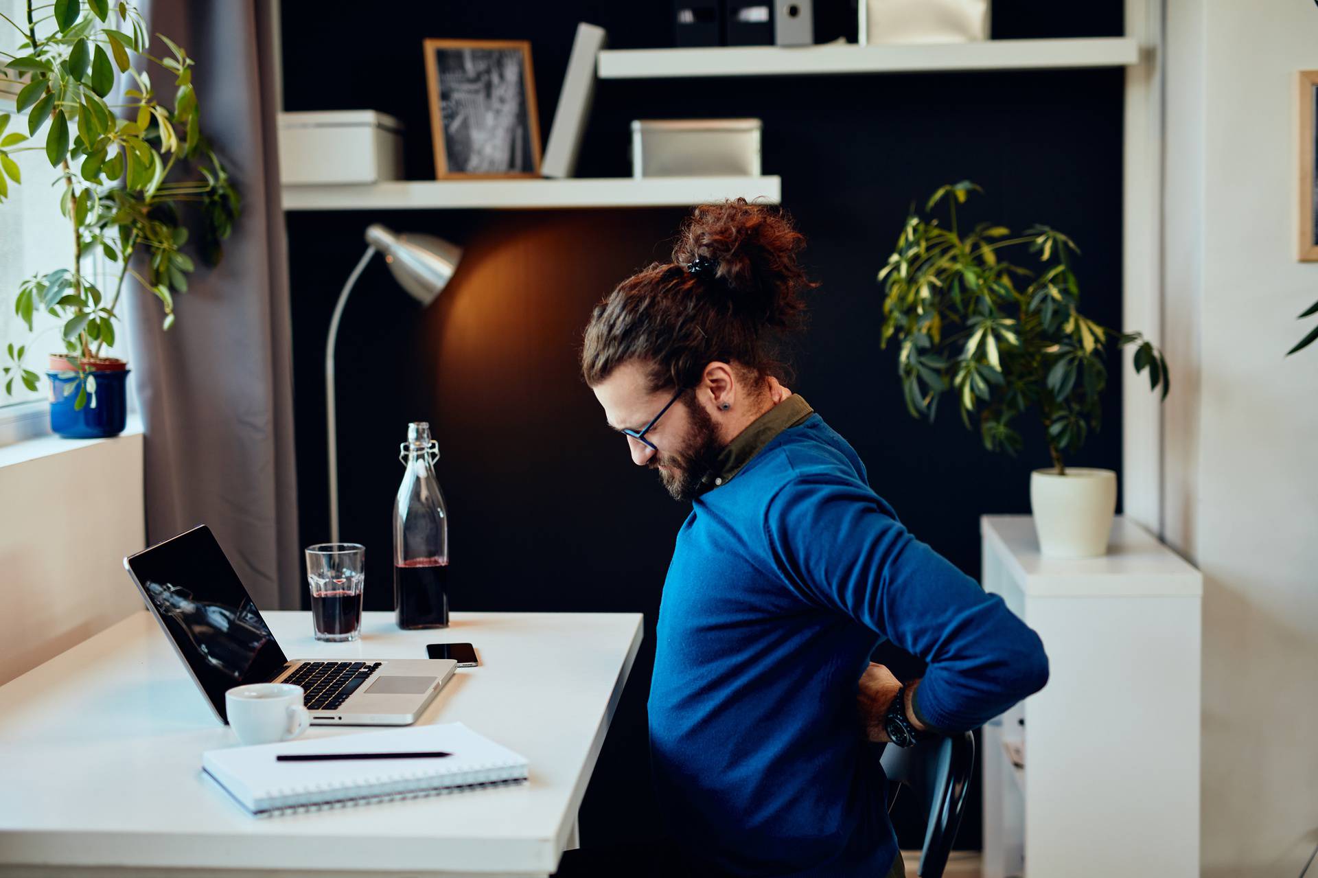 Side view of handsome freelancer sitting in his home office and having back pain.