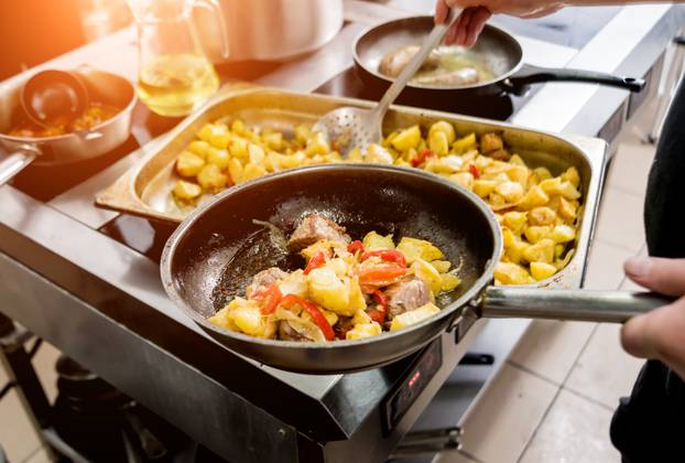 Chef cooks fried potatoes with pieces of meat in a restaurant kitchen