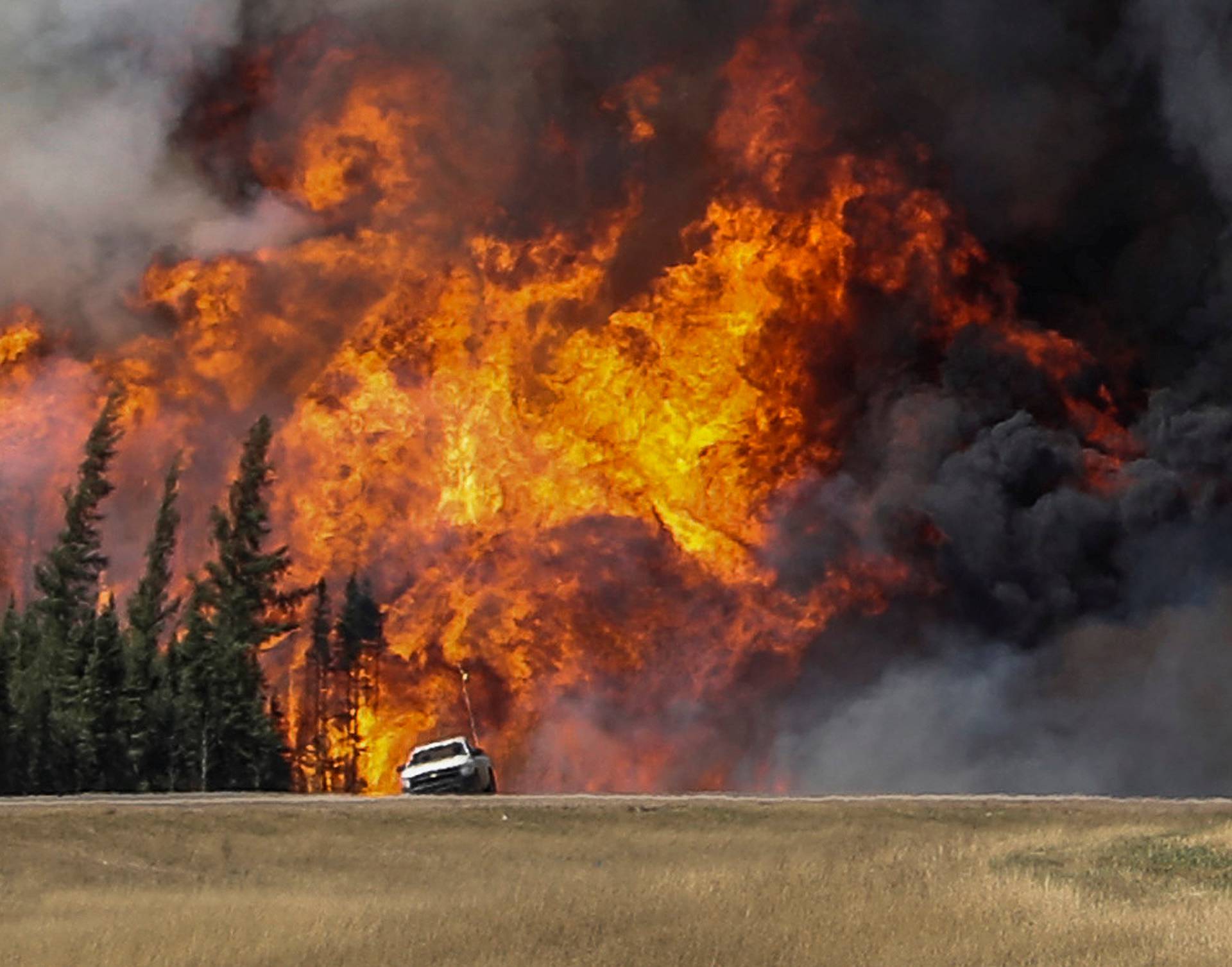 Smoke and flames from the wildfires erupt behind a car on the highway near Fort McMurray