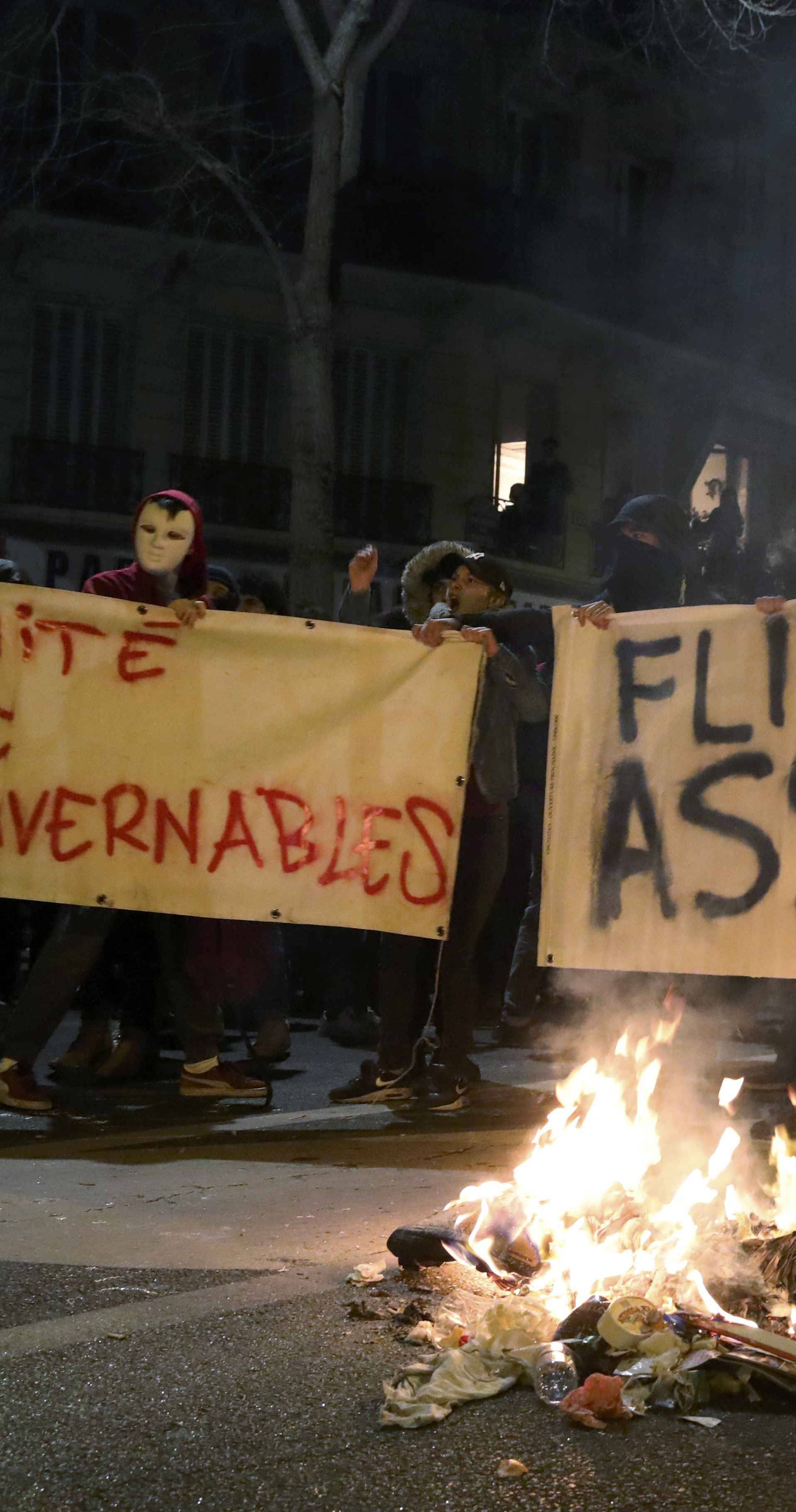 Trash burns on the street as people hold a banners with messages to protest police brutality as they gather at a deomostration in Paris 