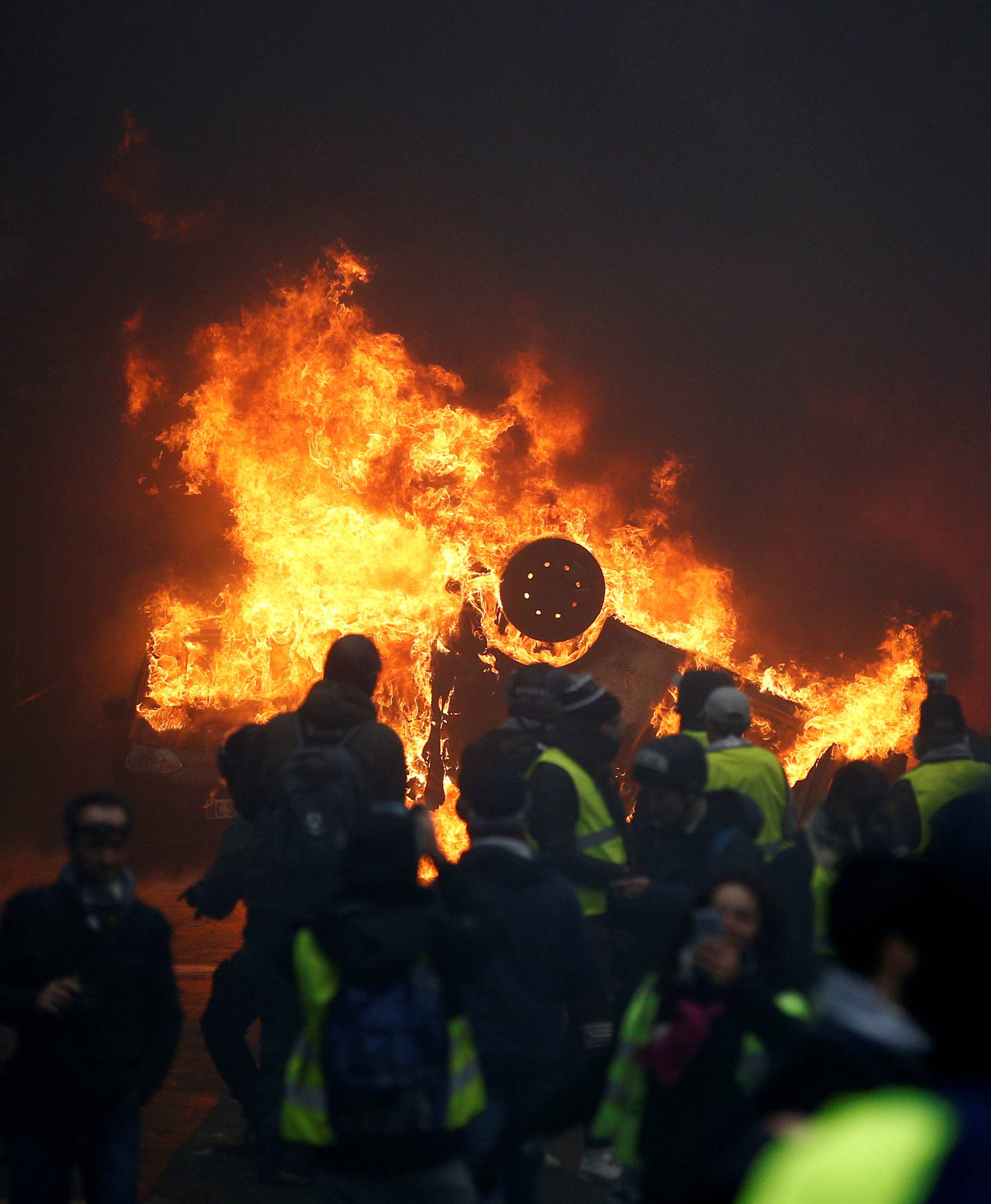 Protesters wearing yellow vests, a symbol of a French drivers' protest against higher diesel fuel taxes, gather near a burning car during clashes near the Place de l'Etoile in Paris