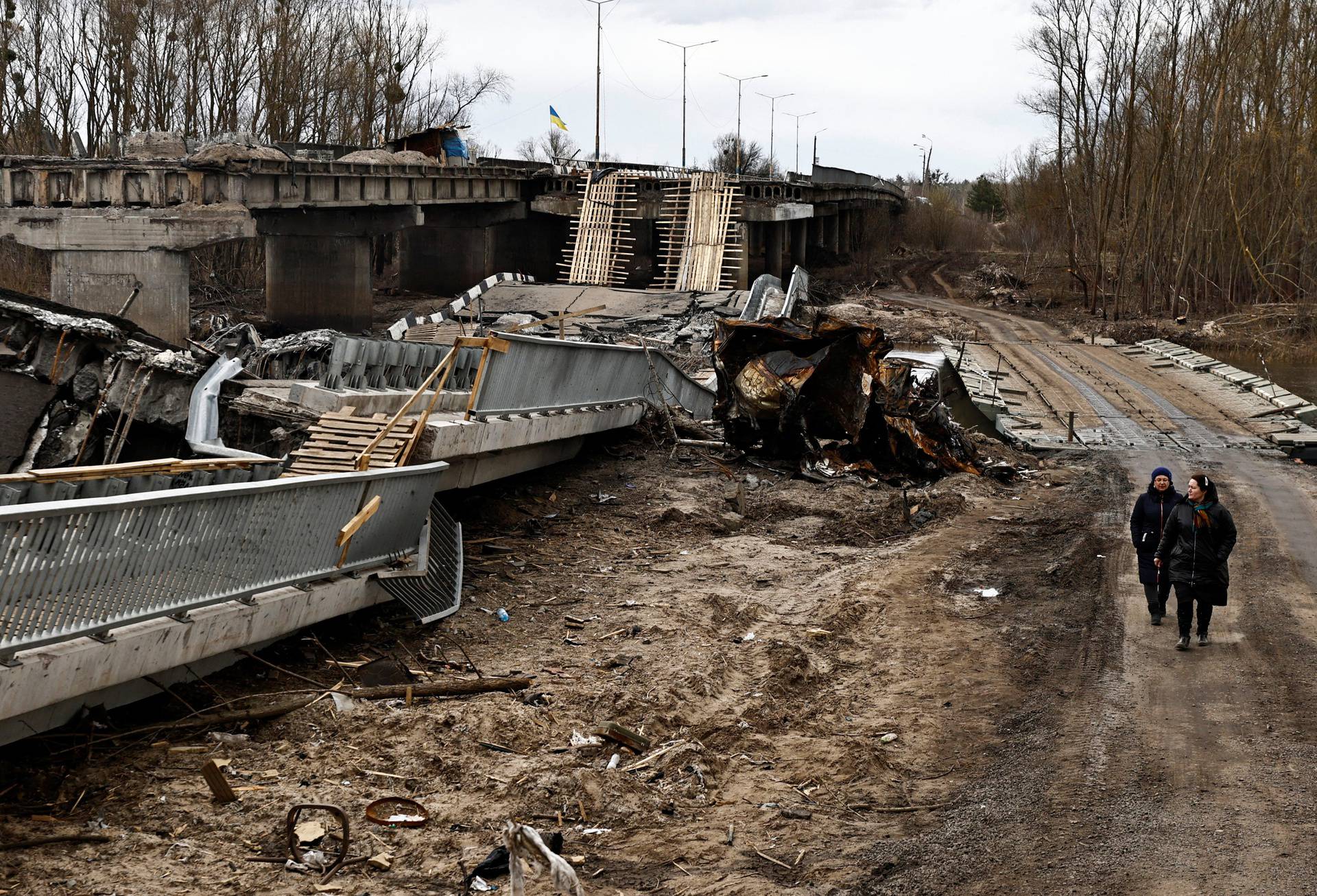 Women walk past a bridge that according to residents was destroyed by Russian army soldiers, in Ivankiv