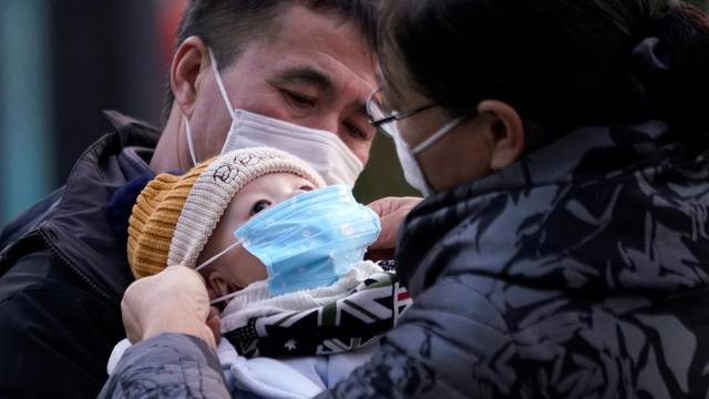 Passengers help a baby wear a mask at the Shanghai railway station