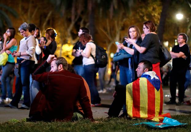 People react as they watch a session of the Catalonian regional parliament on a giant screen at a pro-independence rally in Barcelona