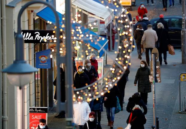 People with protective face masks walk beside Christmas themed lights at Schloss Strasse shopping street in Berlin