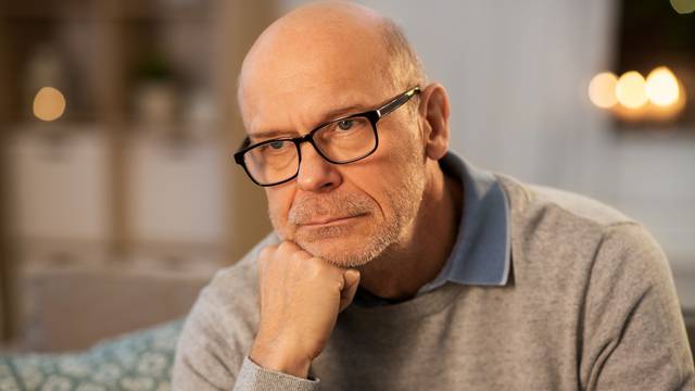 sad senior man in glasses thinking at home