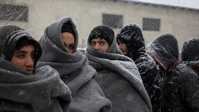 Migrants wait in line to receive free food during a snowfall outside a derelict customs warehouse in Belgrade